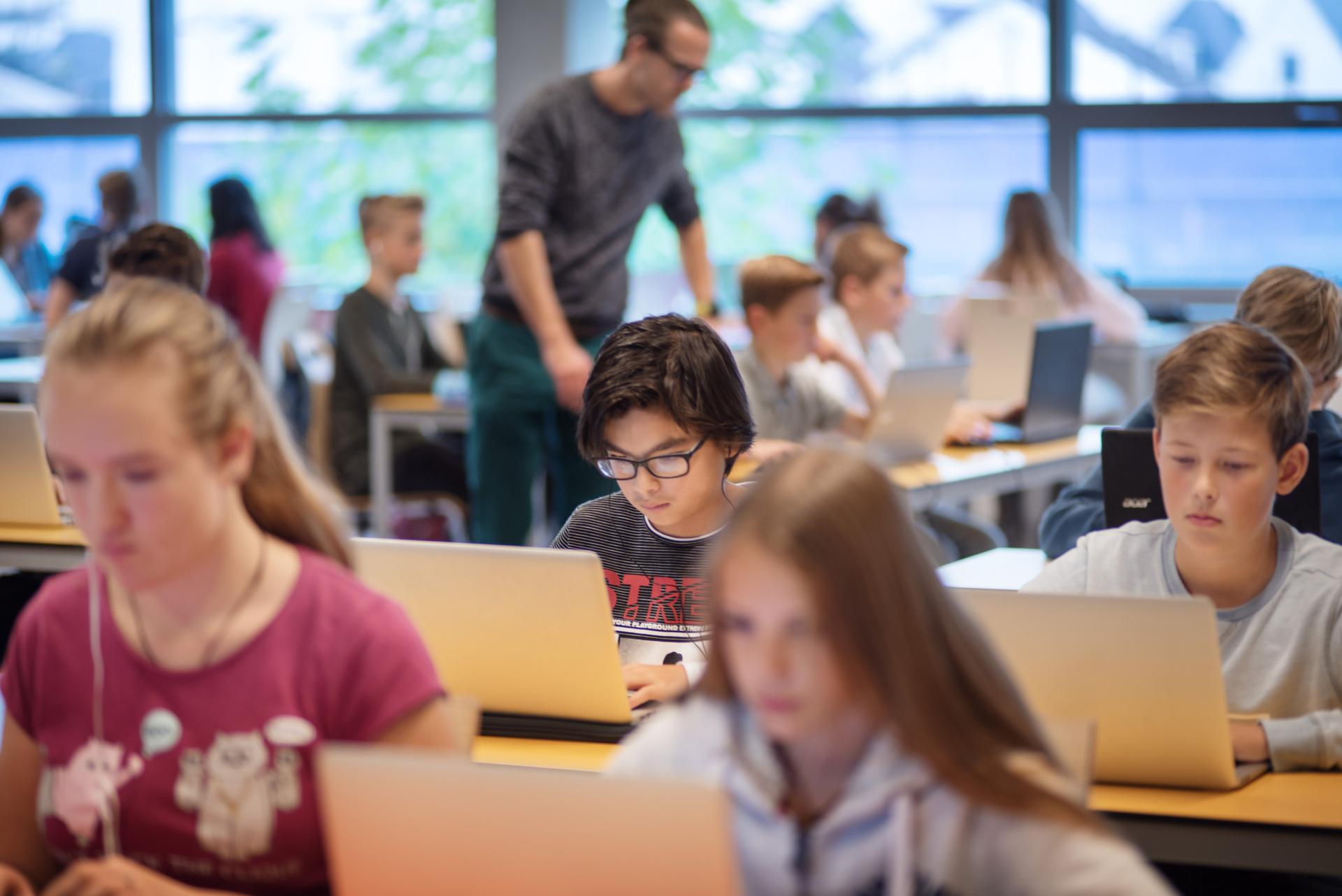 Een klas met kinderen die achter hun laptops zitten.