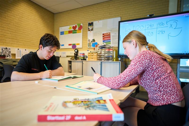 Twee jongeren zijn aan het studeren in een klaslokaal.